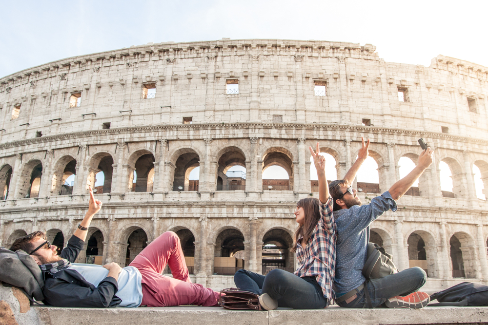 Three,Young,Friends,Tourists,Sitting,Lying,In,Front,Of,Colosseum